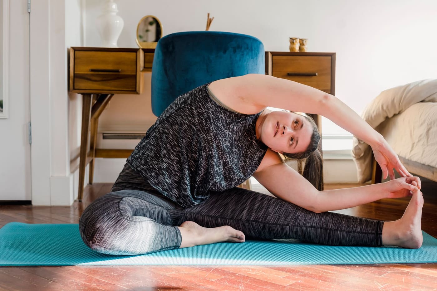 A woman stretching on a teal mat in a home setting