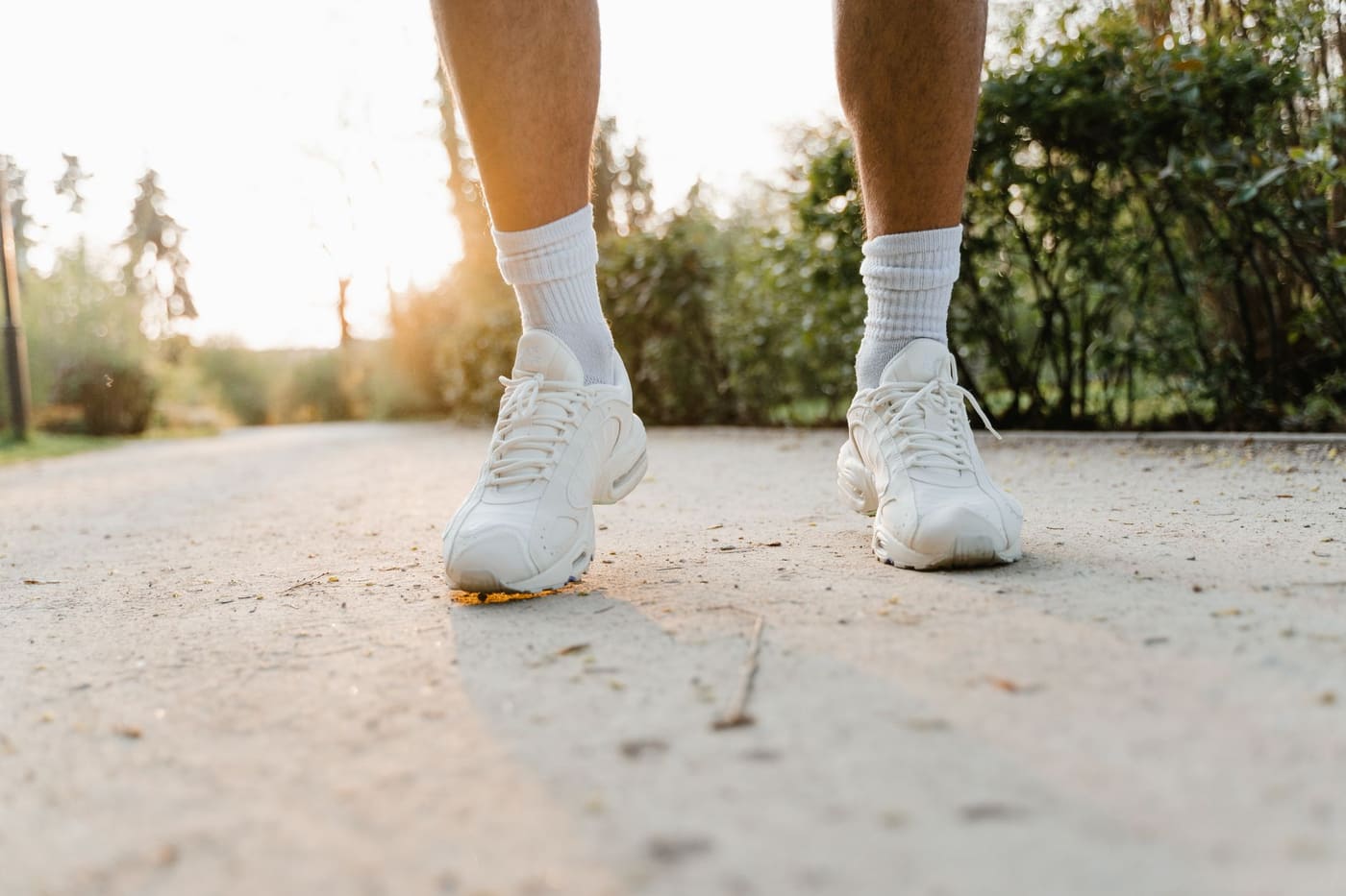 Close-up of legs in white sneakers walking along a sunlit path outdoors